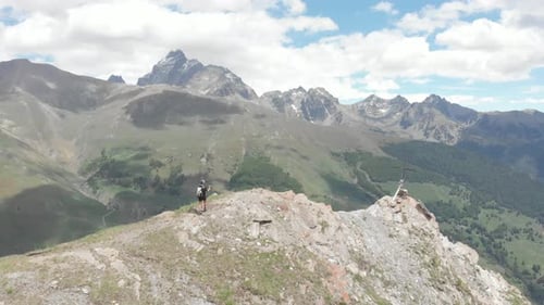 Aerial: Backpacker alpinist hiking to the mountain top, rocky mountain peak dramatic landscape. Summ
