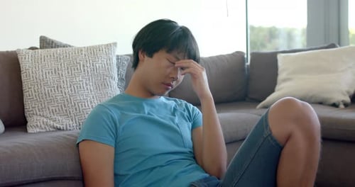 Asian college student sitting on couch, looking tired and stressed