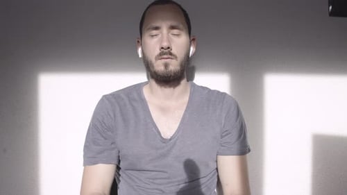 Young man with beard meditating in the morning, listening peaceful music, headphones on, sun shining
