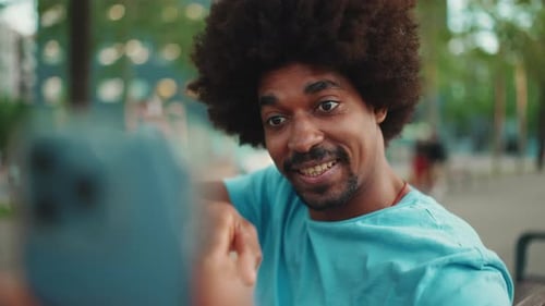 man in blue t-shirt sitting on park bench and talking on speakerphone