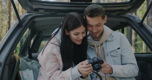 Loving Couple Views Photos in Car Trunk