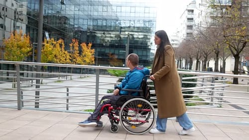 Woman pushing a young man in a wheelchair on a city sidewalk