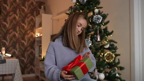 Girl Opens Gift by Christmas Tree Indoors