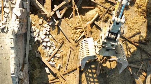 Vue aérienne d'une griffe d'excavatrice manœuvrant sur un sol recouvert de débris lors de la démolition d'un
