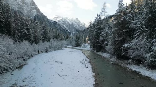 Aerial 4k Drone Footage of a snowy landscape in the Dolomites with a Snow-Covered Forest and River i