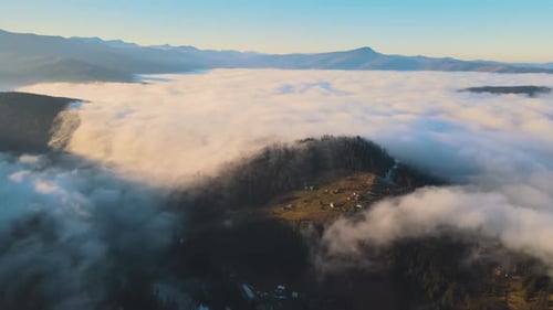 Aerial View of Vibrant Landscape of Foggy Clouds Covering Mountain Hills and Small Scattered Village