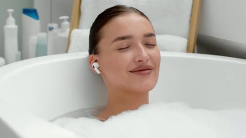 Relaxing woman in bubble bath listens to music