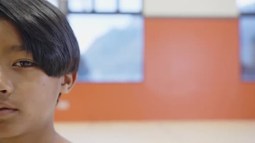 Smiling boy in school gymnasium with red wall and windows in background