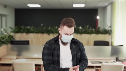 Bearded handsome male office worker applies antiseptic spray on hands and carefully rubs