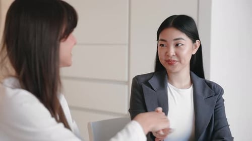 Smiling Businesswomen Shaking Hands Warmly While Seated in Bright Minimalist Office Sealing