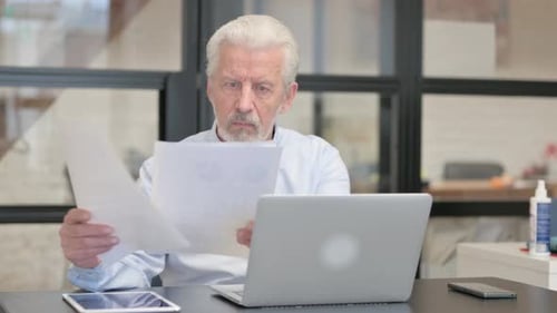 Senior Man Reads Document in Modern Office