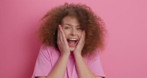 Excited woman with curly hair smiling on pink