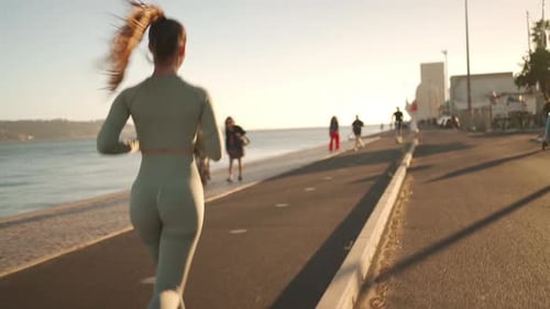 Following Shot of Young Woman in Sportswear Confidently Running on Embankment