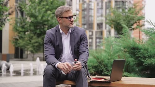 Erwachsener Mann sitzt auf einer Bank und arbeitet mit Laptop und hält eine Flasche Wasser in Zeitlupe