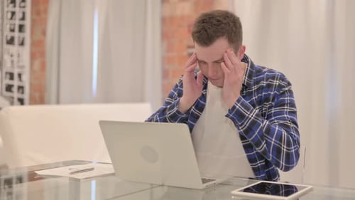 Young Adult Rubbing Temples While Working on Laptop