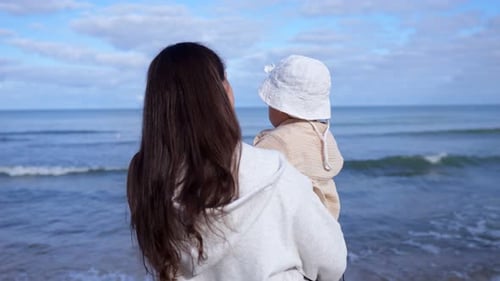 Mommy Carefully Holds Daughter in Arms Watching Sea Waves