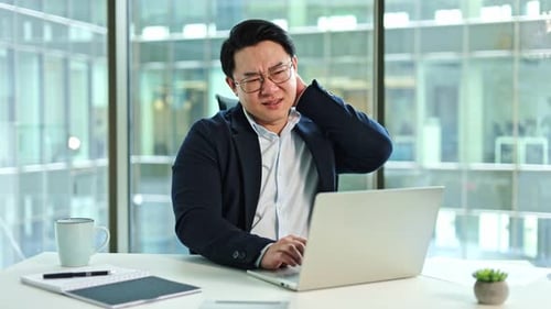 Tired Businessman Suffering From Neck Pain While Working on Laptop in Office