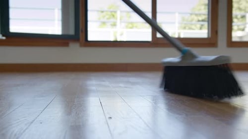 Broom sweeping across wood floor in bright room
