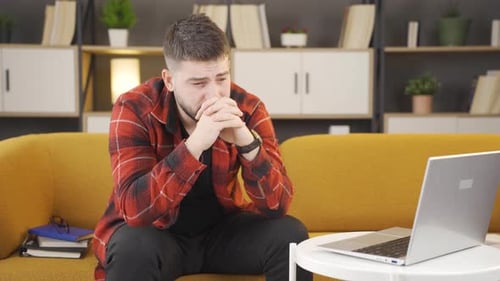 Man Sitting Thoughtfully on Couch with Laptop
