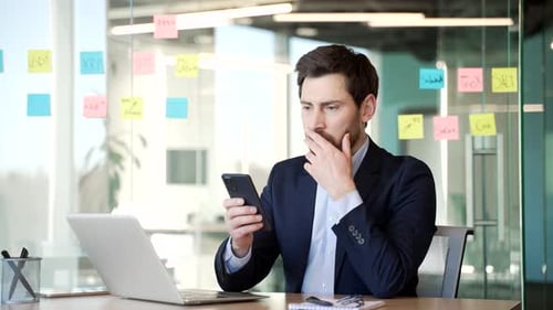 Man in Suit Looking at Mobile Phone in Office
