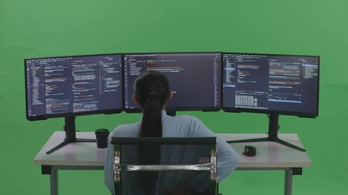 Rückansicht einer Entwicklerin mit Rückenschmerzen beim Schreiben von Code mit mehreren Bildschirmen auf grünem Bildschirm