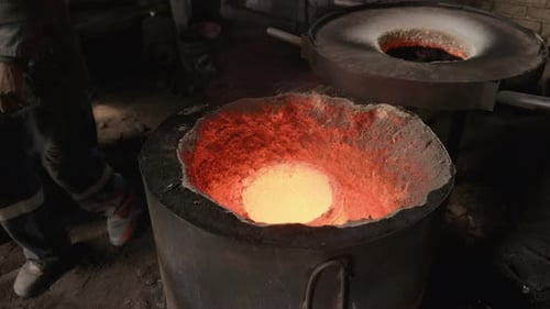 Wide Slow motion of a open furnace pot in a rustic foundry factory with worker passing the furnace