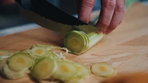 Chef slicing green vegetables on a wooden board with precision for culinary preparation