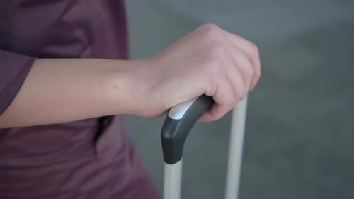 Mão segurando a alça da mala com rodinhas durante a viagem para fora do aeroporto