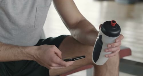 Portrait of a guy in a gym while resting between a workout and the other uses his phone to watch s
