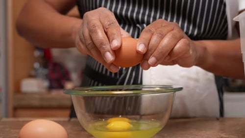 Cracking organic free-range eggs into a glass bowl to mix and add to a homemade recipe - side view i