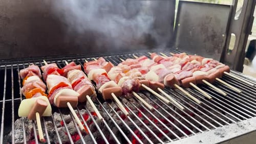 Handvideo von Fleischspießen, die auf einem Holzkohlegrill gegrillt werden, mit roten Paprika, weißen Zwiebeln und