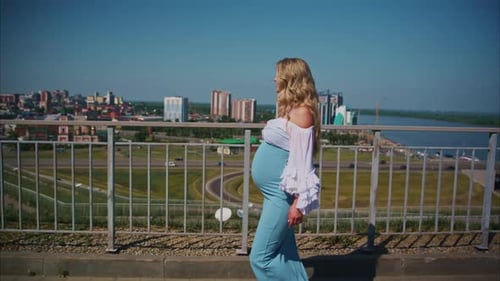 Pregnant Woman Walks Rooftop Overlooking City on Sunny Day