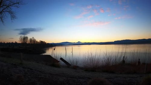 Time Lapse of a beautiful sunrise, scenic view of a meadow next to a large lake, big boat passing ov