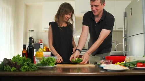 A young woman wearing an apron stands in front of the kitchen counter and her smiling boyfriend