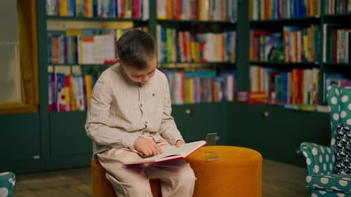 in Bookstore in the Children Area a Handsome Little Boy in Light Clothes Reads a Book