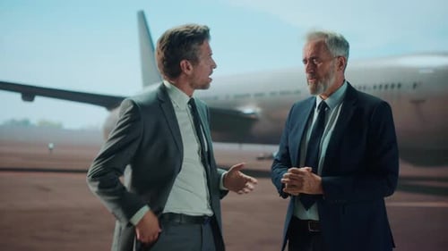 Zwei Geschäftsleute in Anzügen diskutieren in der Nähe eines Flugzeugs auf dem Rollfeld.