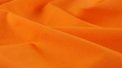 Close-up view of the soft folds of the cadmium orange cotton fabric. The textile background rotates