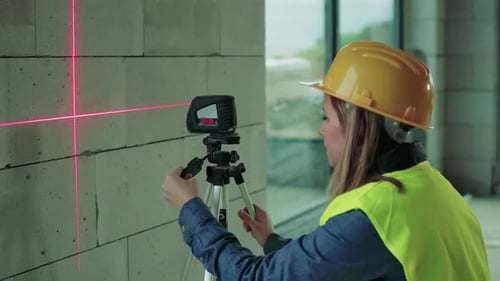 Young Woman Worker with Laser on the Building Site
