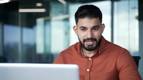 Confident businessman talking on a video call conference using laptop sitting at workplace in office