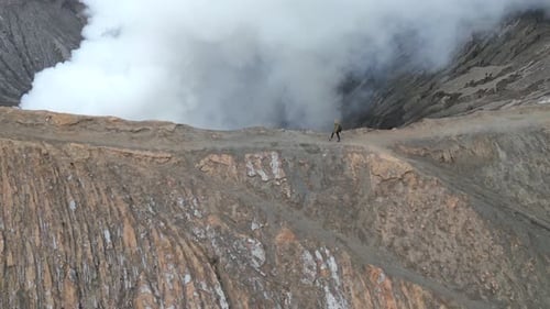Woman Walking Along the Rim of Steaming Mount Bromo Volcano Crater in Indonesia
