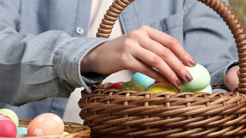 Frau legt bemalte Eier in den Osterkorb am Tisch drinnen, Nahaufnahme