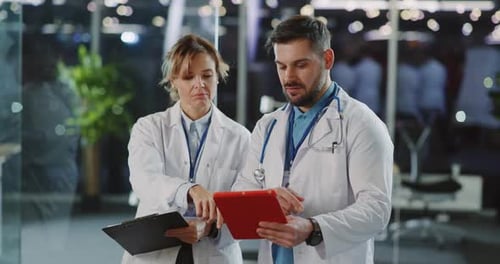 Couple of Professional Medic Workers in Lab Coats Discussing Common Patients Using Tablet Computer