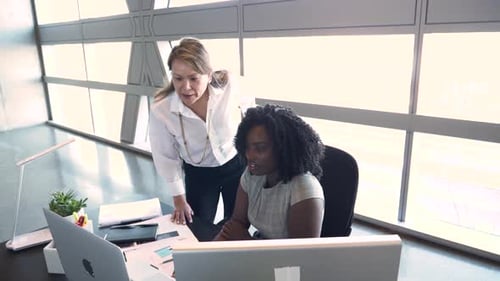 Mature businesswomen collaborate at laptop in modern office setting