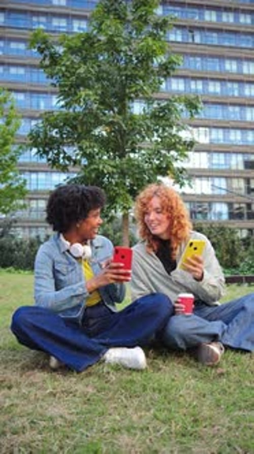 Two Young Women Using Phones in Urban Park