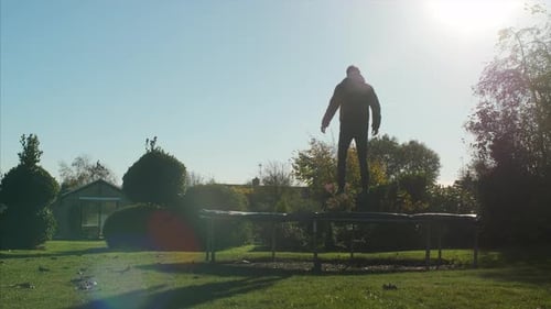 A man jumping on a trampoline and doing a simple trick. WIDE STATIC SHOT with LENS FLARE.