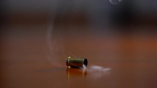 Eine Patronenhülse fällt in Zeitlupe auf eine Holzoberfläche, das gebrannte Messinggehäuse prallt hinterher