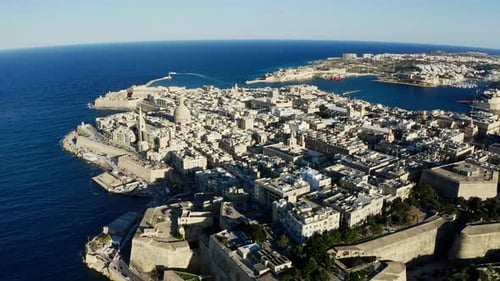Aerial orbiting left wide shot of old town Valletta during sunset with maltese colors, Malta