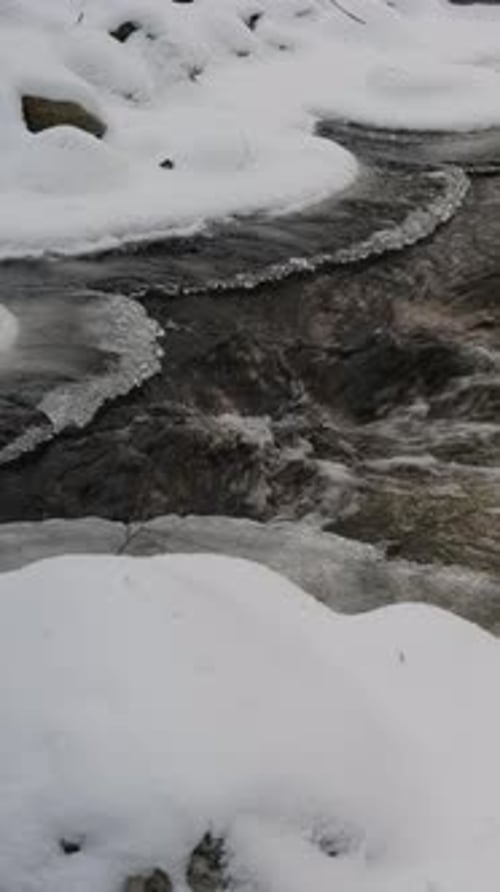 Gros plan d'un ruisseau traversant un paysage enneigé à la fin de l'hiver.