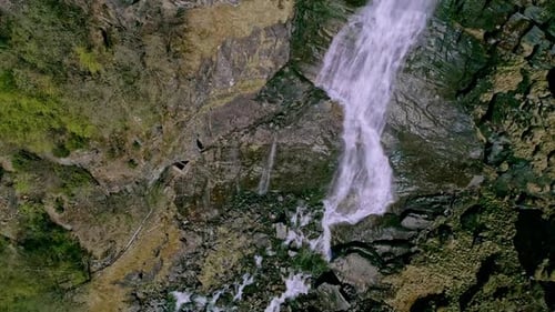 Top down shot over waterfalls along rocky mountain cliff at daytime.