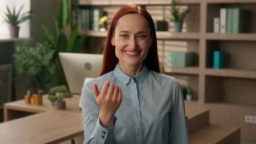 Smiling Woman Beckons Toward the Camera in Office